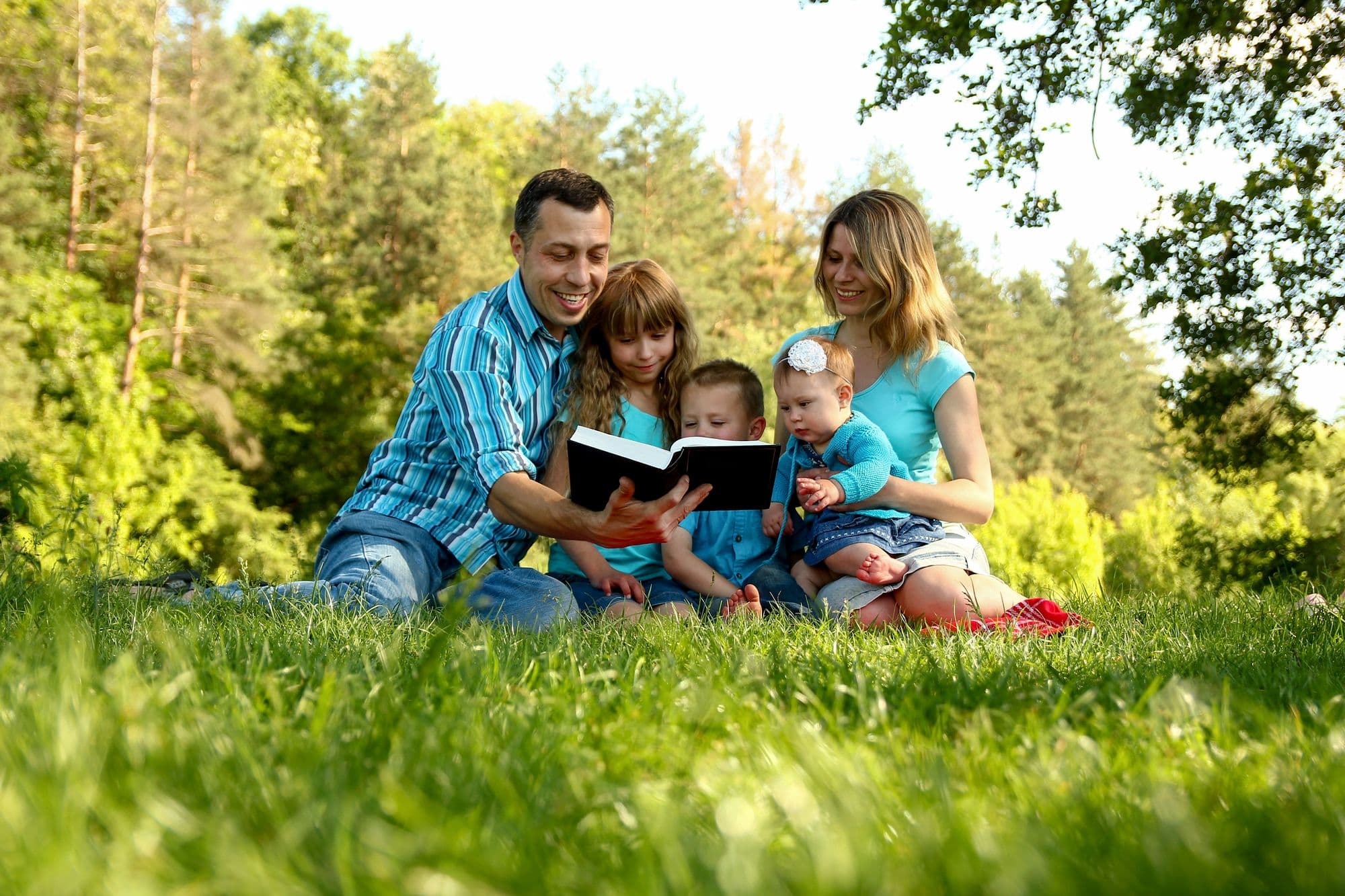 Family sitting on the grass reading the Bible together
