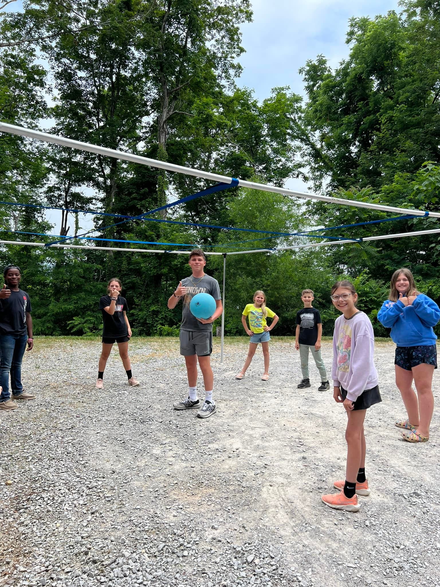 Campers playing volleyball on a gravel court