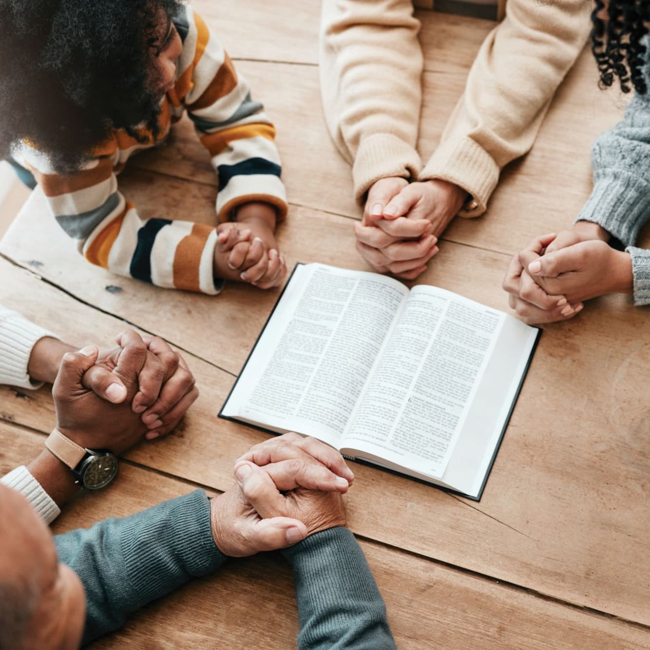 Family holding hands in prayer around an open Bible