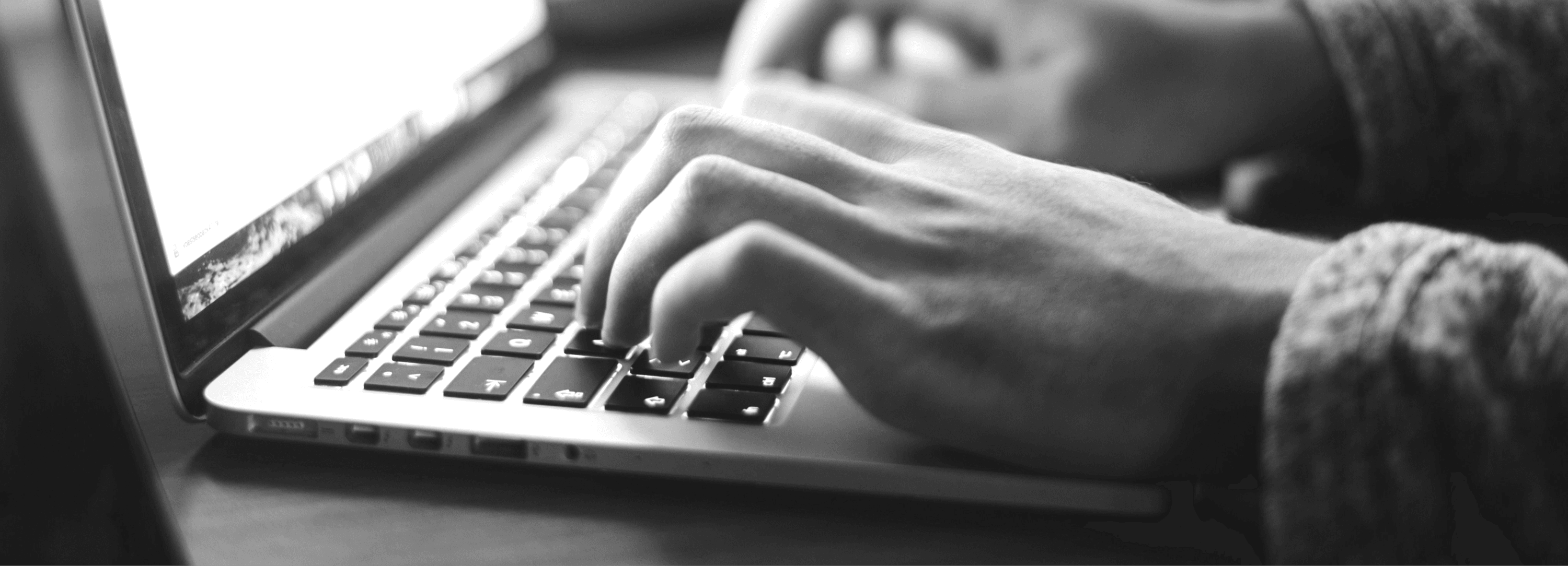 Hands typing on a laptop keyboard in black and white