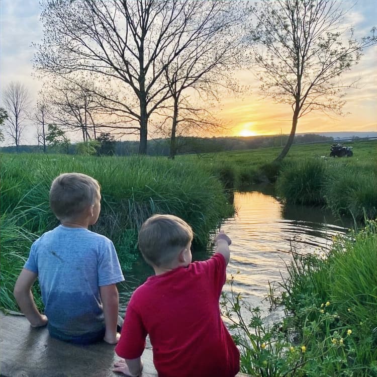 Two boys sitting by a creek at sunset on the farm