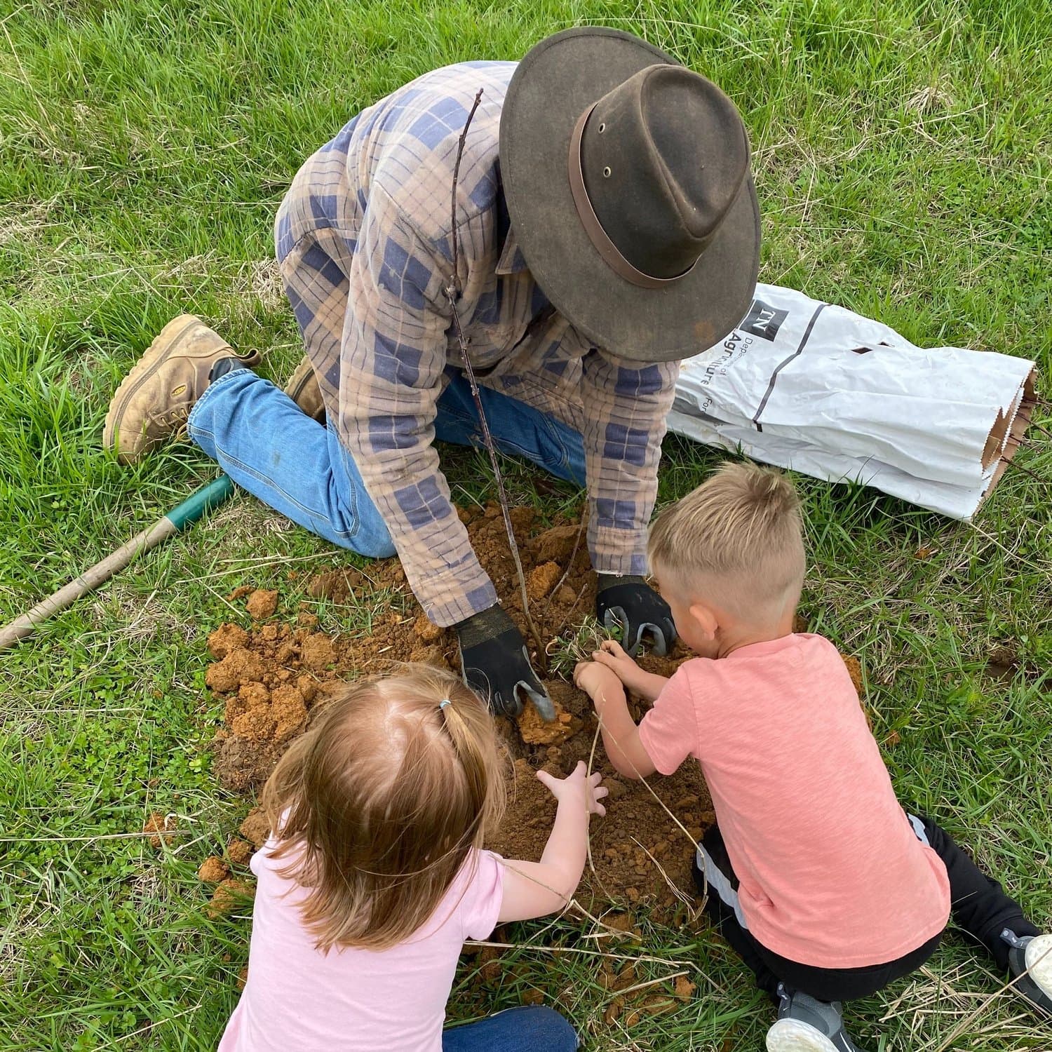 Farmer teaching two young children to plant in the soil