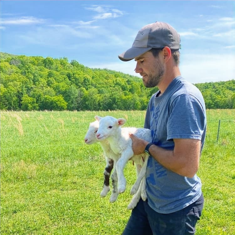 Young farmer carrying a lamb across the pasture