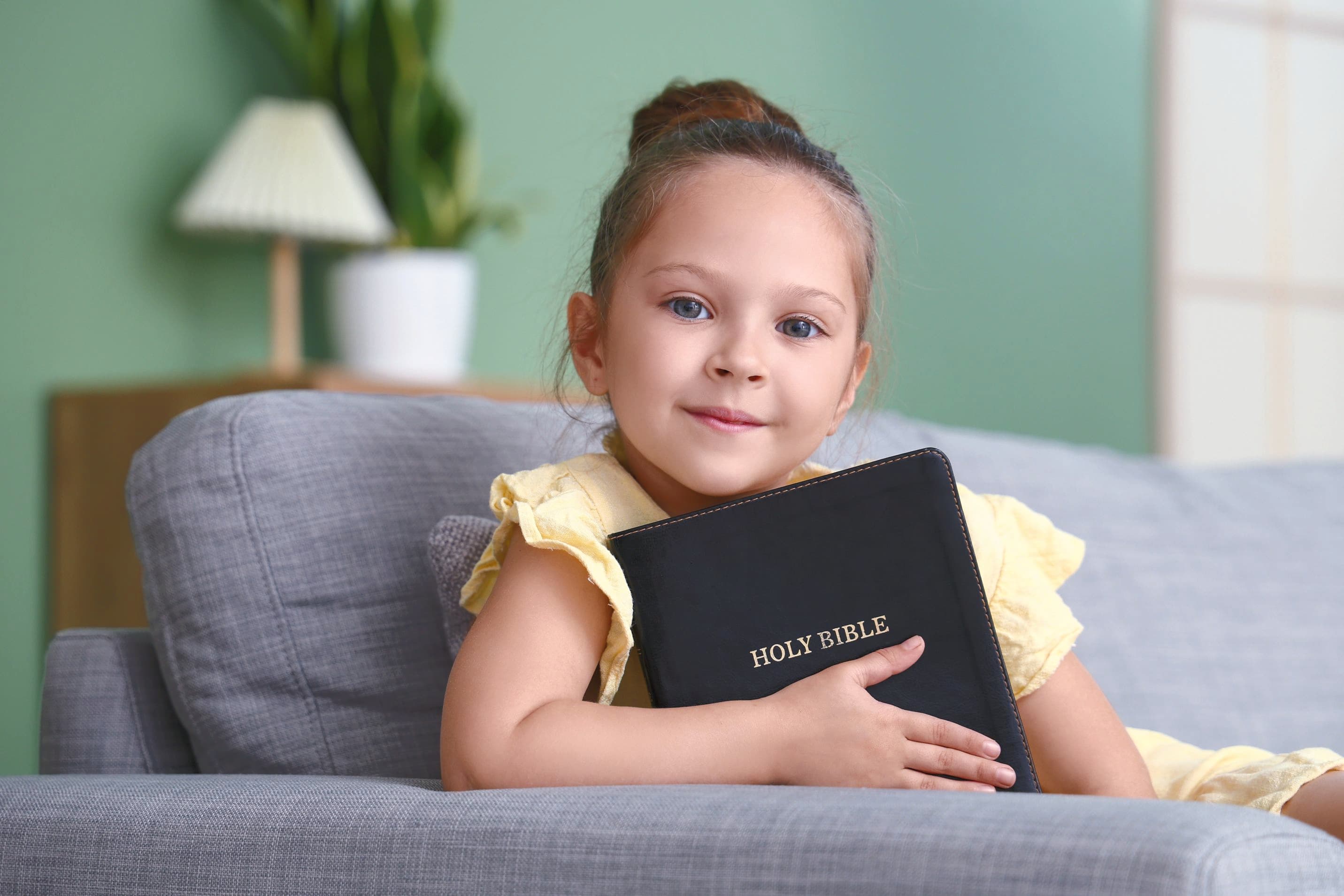 Young girl hugging a Holy Bible while sitting on a couch